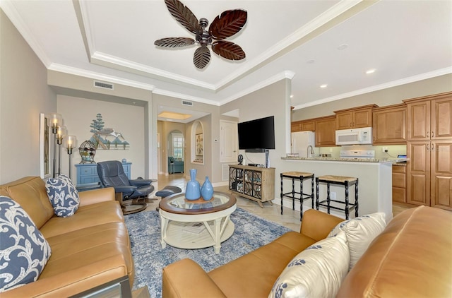 tiled living room with ceiling fan, crown molding, and a raised ceiling