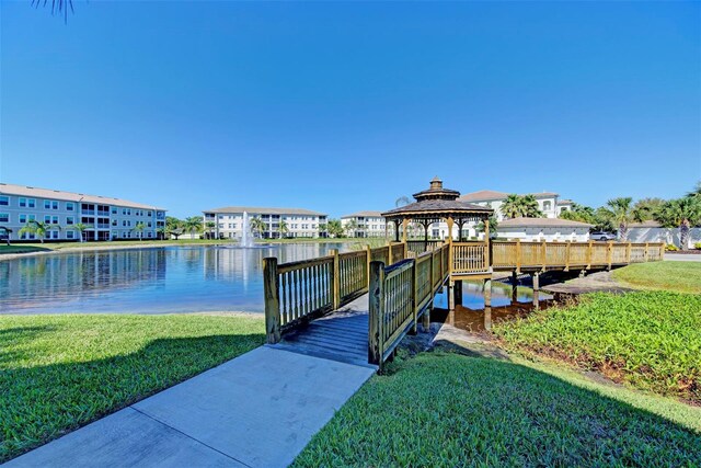 dock area with a gazebo, a water view, and a lawn