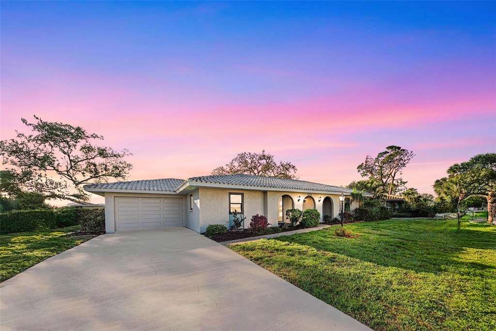 ranch-style house with driveway, a garage, a tile roof, a yard, and stucco siding