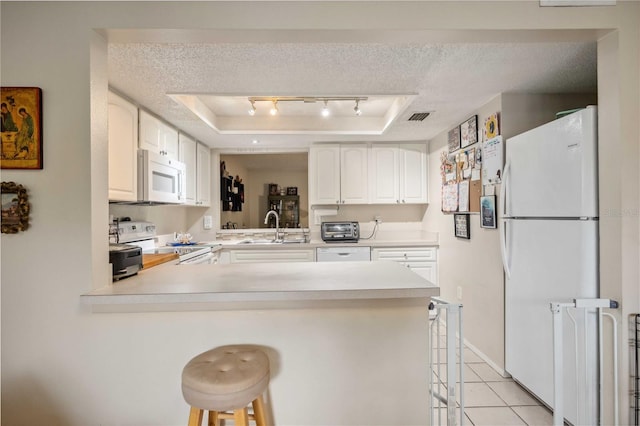 kitchen featuring white appliances, white cabinets, kitchen peninsula, a breakfast bar area, and a tray ceiling