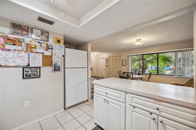 kitchen featuring light tile patterned floors, a textured ceiling, white cabinets, and white fridge