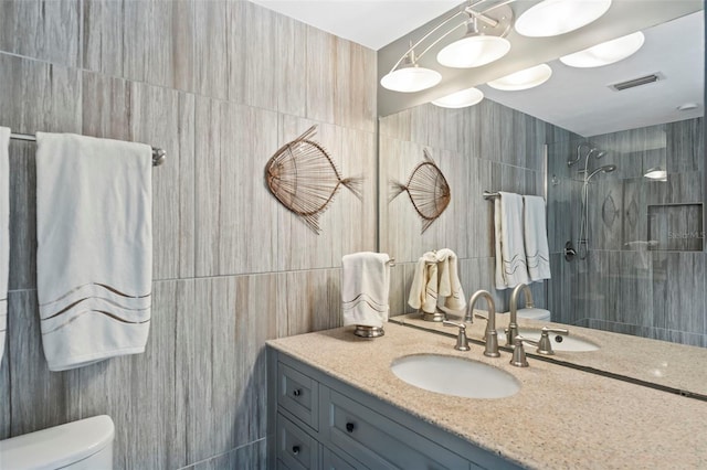 bathroom with toilet, a shower, tile walls, and vanity