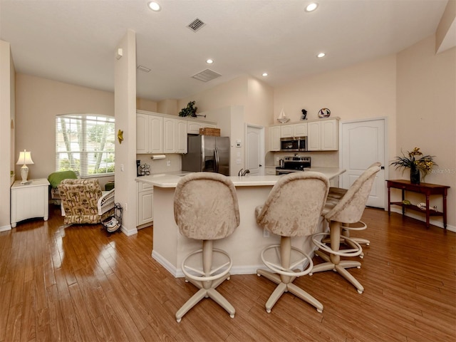 kitchen featuring hardwood / wood-style flooring, a kitchen breakfast bar, white cabinetry, and appliances with stainless steel finishes