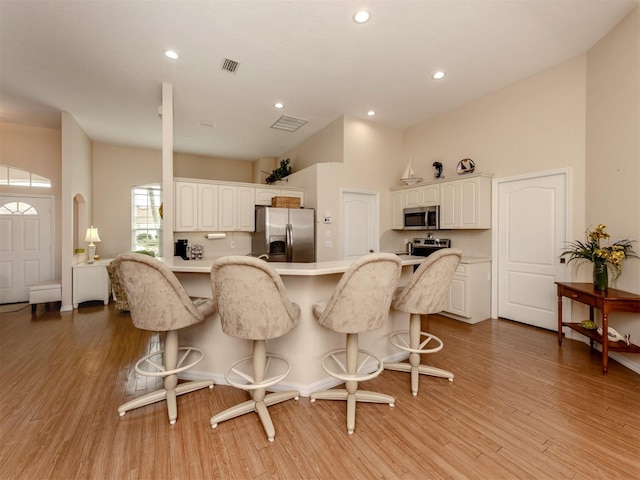 kitchen featuring white cabinetry, a breakfast bar, a kitchen island, light hardwood / wood-style floors, and stainless steel appliances