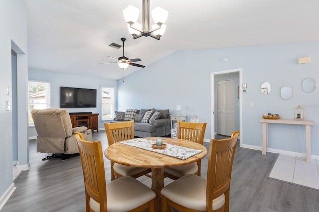 dining space with dark wood-type flooring, ceiling fan with notable chandelier, and vaulted ceiling