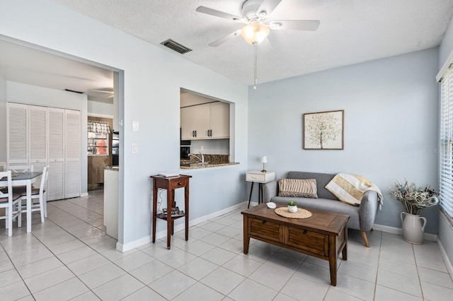 living room with ceiling fan, a textured ceiling, and light tile patterned floors