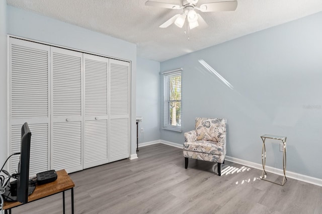 living area with ceiling fan, a textured ceiling, and light hardwood / wood-style flooring