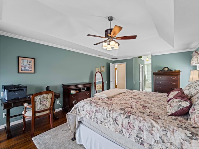 bedroom with ceiling fan, connected bathroom, a raised ceiling, dark hardwood / wood-style flooring, and ornamental molding