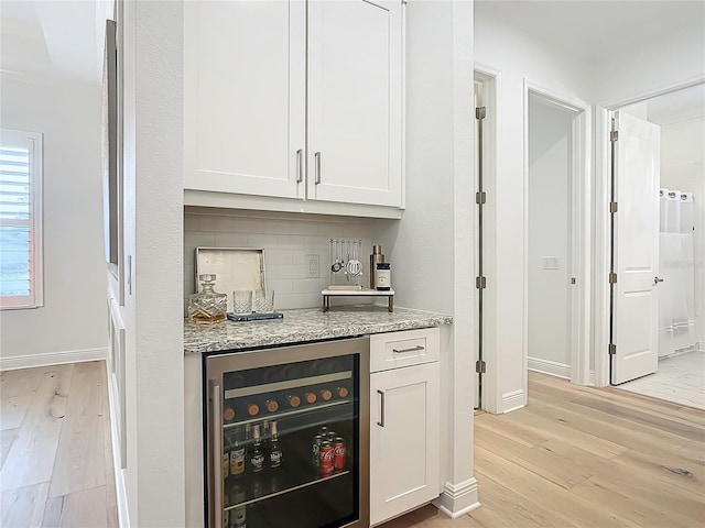 bar featuring wine cooler, white cabinetry, light stone countertops, and light wood-type flooring