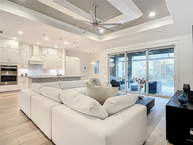 living room featuring sink, crown molding, ceiling fan, light hardwood / wood-style floors, and a raised ceiling