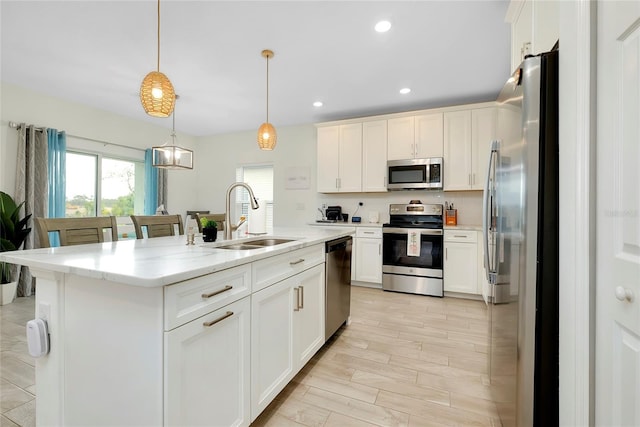 kitchen with sink, hanging light fixtures, stainless steel appliances, light stone countertops, and a center island with sink