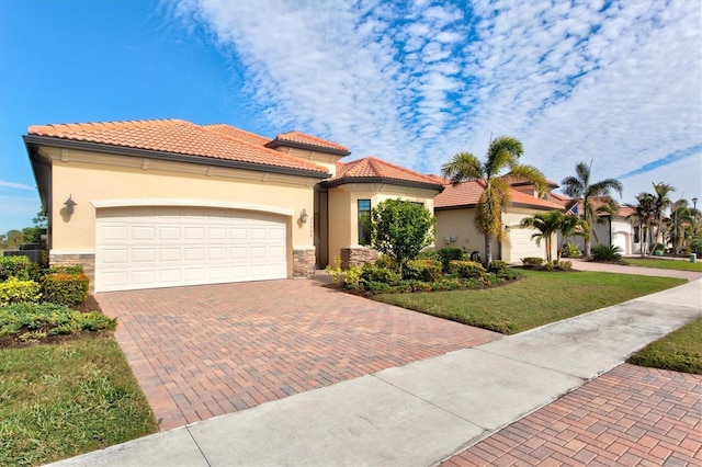 mediterranean / spanish house featuring stone siding, an attached garage, decorative driveway, a front lawn, and stucco siding