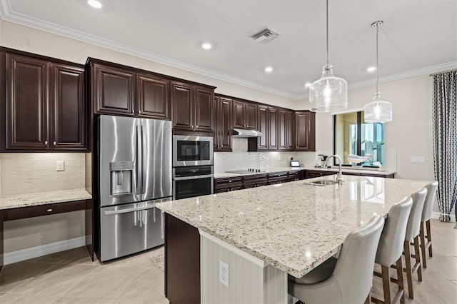 kitchen featuring sink, appliances with stainless steel finishes, a kitchen island with sink, hanging light fixtures, and light stone countertops