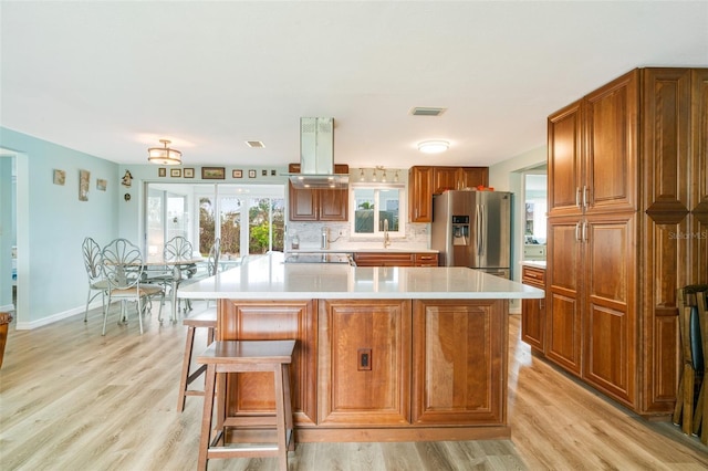 kitchen featuring a kitchen island, light hardwood / wood-style floors, a kitchen breakfast bar, backsplash, and stainless steel fridge