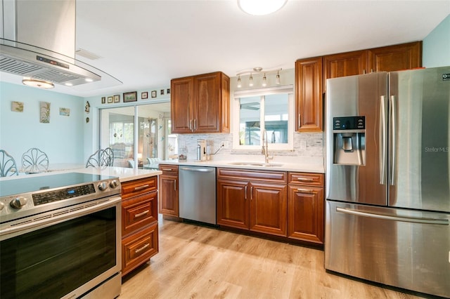 kitchen featuring decorative backsplash, island range hood, sink, light wood-type flooring, and stainless steel appliances