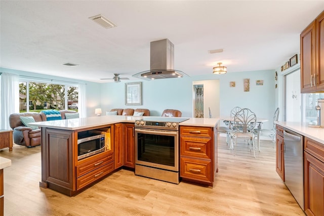 kitchen featuring kitchen peninsula, ceiling fan, light wood-type flooring, island range hood, and stainless steel appliances