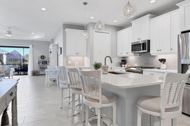 12488 Palatka Dr, Venice, FL 34293 - kitchen with sink, hanging light fixtures, appliances with stainless steel finishes, an island with sink, and white cabinets