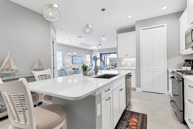 12488 Palatka Dr, Venice, FL 34293 - kitchen with sink, appliances with stainless steel finishes, a kitchen island with sink, white cabinetry, and decorative light fixtures