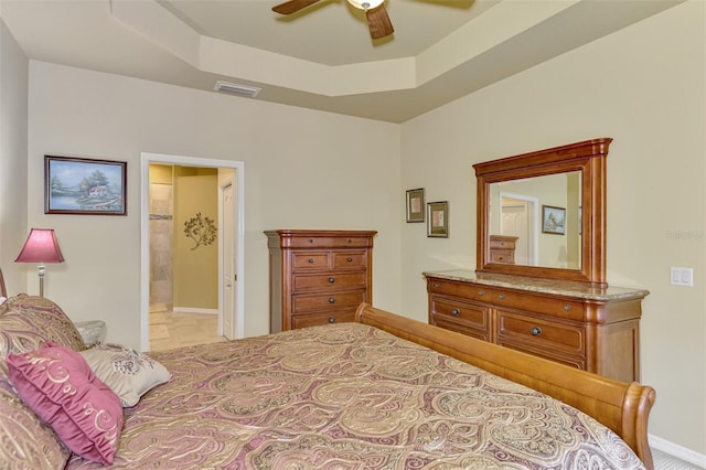 bedroom with a raised ceiling, ceiling fan, and connected bathroom