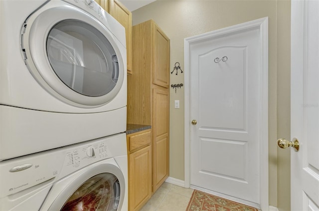 clothes washing area featuring stacked washer / dryer, light tile patterned floors, and cabinets