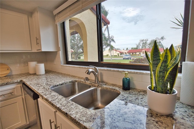 kitchen with light stone countertops, white cabinets, decorative backsplash, sink, and stainless steel dishwasher