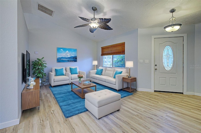 living room featuring ceiling fan, vaulted ceiling, light hardwood / wood-style flooring, and a textured ceiling