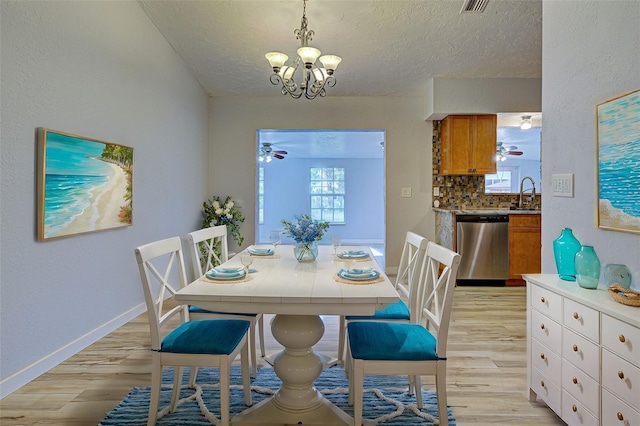 dining space featuring sink, light hardwood / wood-style floors, a textured ceiling, and a notable chandelier