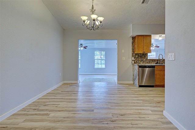 unfurnished dining area featuring sink, ceiling fan with notable chandelier, a textured ceiling, and light wood-type flooring