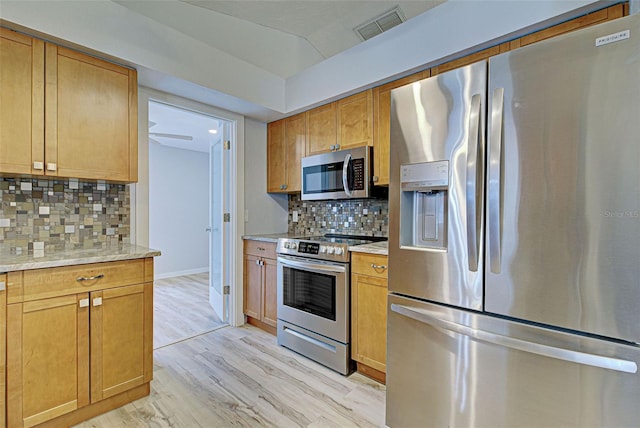 kitchen featuring appliances with stainless steel finishes, tasteful backsplash, lofted ceiling, light hardwood / wood-style floors, and light stone countertops