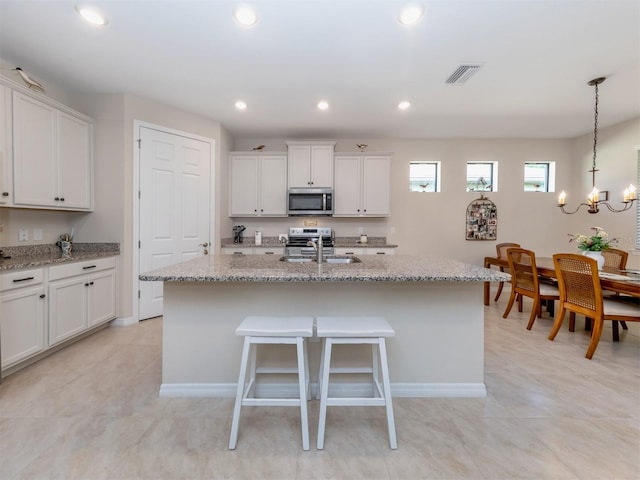 kitchen with white cabinetry, an island with sink, sink, hanging light fixtures, and light stone counters