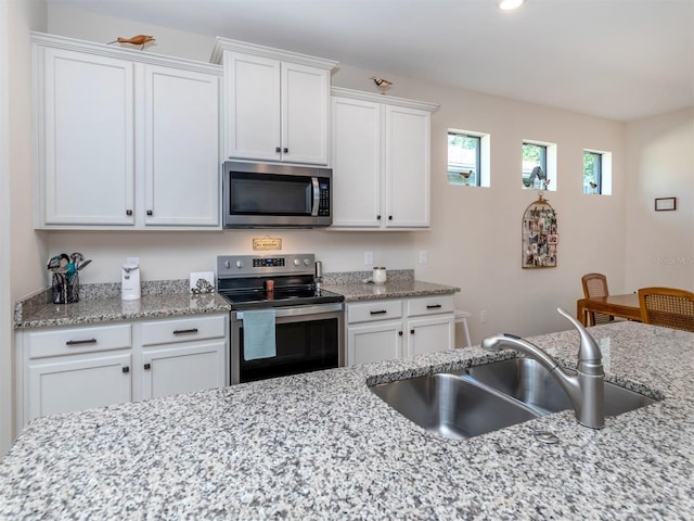 kitchen with appliances with stainless steel finishes, white cabinetry, light stone counters, and sink