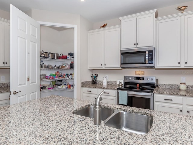 kitchen with light stone counters, sink, white cabinetry, and appliances with stainless steel finishes