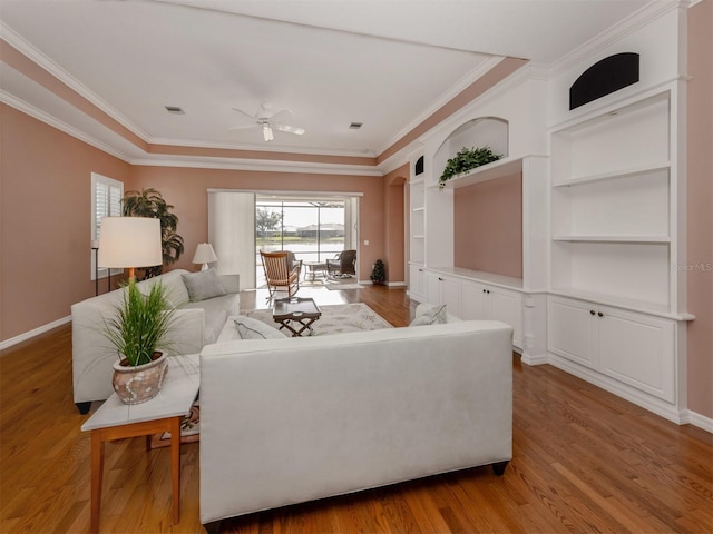 living room with crown molding, built in shelves, ceiling fan, and light hardwood / wood-style flooring