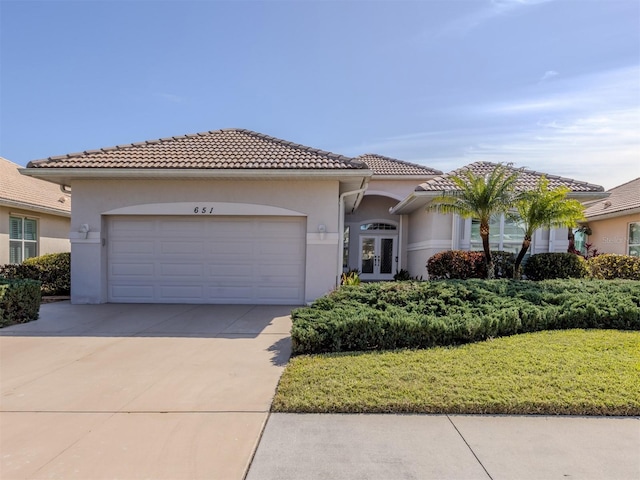 mediterranean / spanish-style house with a garage, a front lawn, and french doors