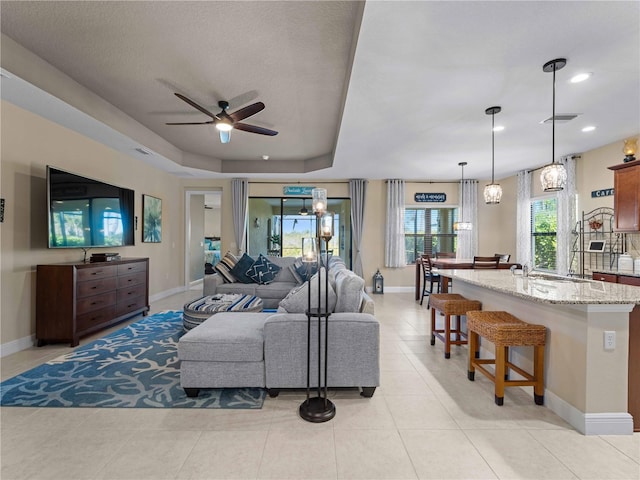 tiled living room featuring a raised ceiling and ceiling fan