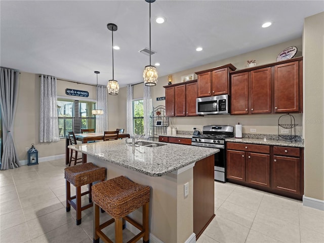 kitchen with stainless steel appliances, pendant lighting, a center island with sink, and light stone counters