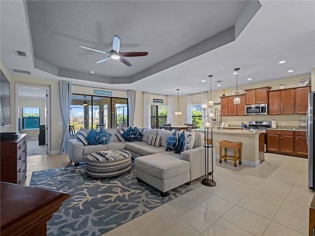 living room with a raised ceiling, light tile patterned floors, a textured ceiling, and ceiling fan