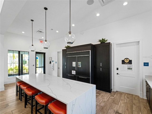 kitchen with paneled fridge, decorative light fixtures, a breakfast bar area, a center island, and light stone countertops