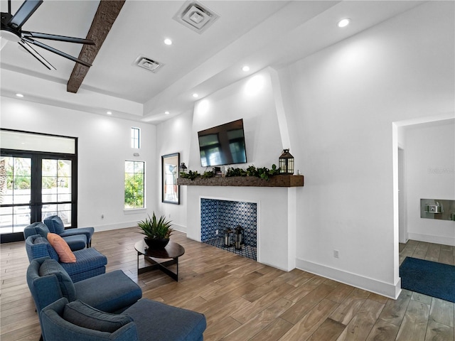 living room featuring french doors, hardwood / wood-style floors, a tile fireplace, and a high ceiling