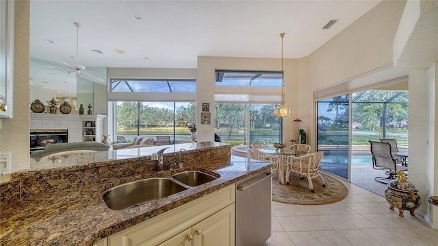 kitchen with sink, dark stone countertops, stainless steel dishwasher, a fireplace, and cream cabinetry