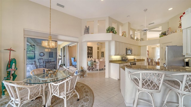 dining area with light tile patterned flooring, a towering ceiling, and ceiling fan with notable chandelier