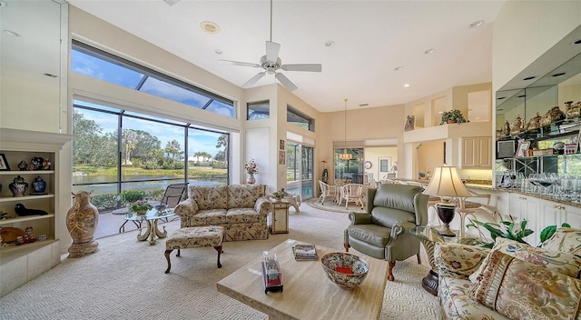 carpeted living room featuring ceiling fan, a high ceiling, and a water view