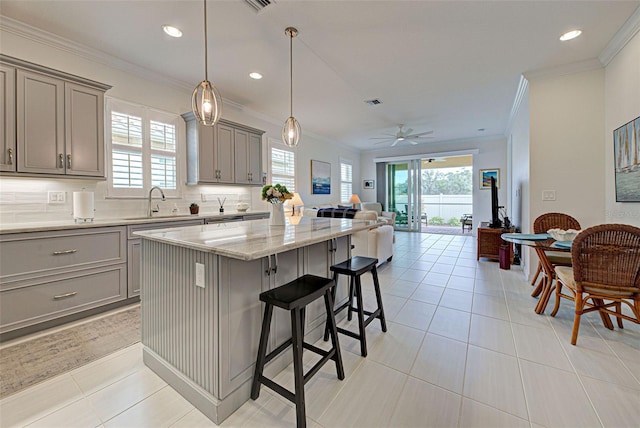 kitchen featuring backsplash, a center island, ornamental molding, a kitchen bar, and decorative light fixtures