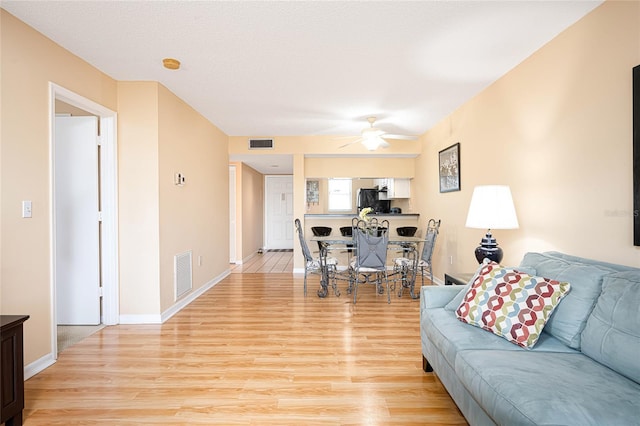 living room with a textured ceiling, ceiling fan, and light wood-type flooring