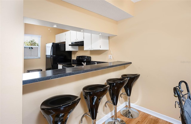 kitchen with white cabinets, light hardwood / wood-style floors, and black appliances