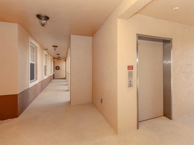 hallway with elevator and light carpet