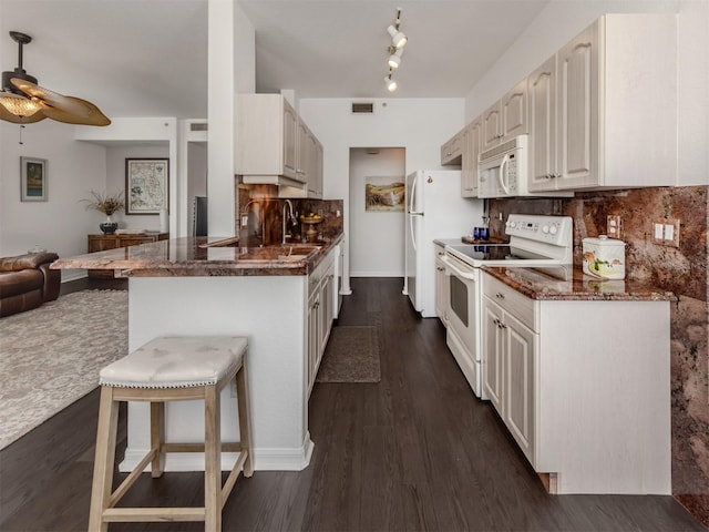 kitchen featuring white appliances, tasteful backsplash, dark stone countertops, kitchen peninsula, and a breakfast bar area