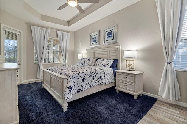 bedroom featuring a tray ceiling, wood finished floors, a ceiling fan, and baseboards