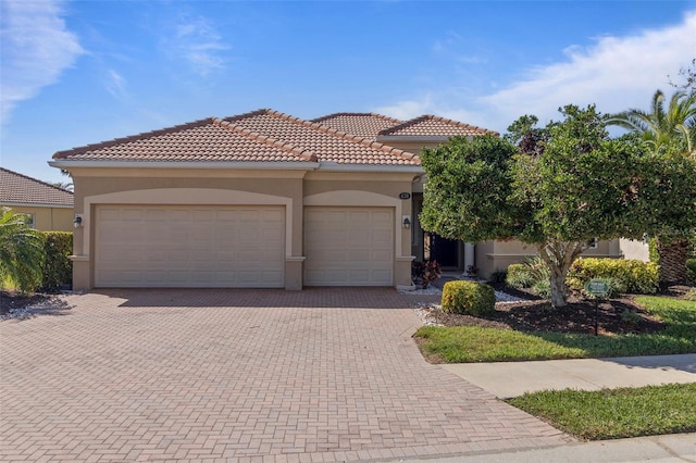 mediterranean / spanish house with a garage, decorative driveway, a tiled roof, and stucco siding