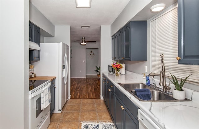 kitchen featuring sink, white appliances, light tile patterned floors, blue cabinetry, and ceiling fan